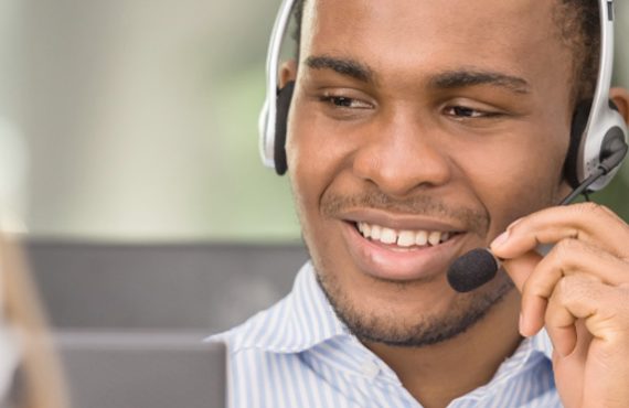 A smiling man, wearing a headset, smiles.